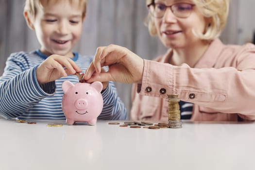 three years old child and young woman sitting at the table with money and piggybank. Happy boy with euro coins. Future childhood and education investment. Finance and savings concept. Son playing with mother