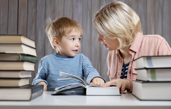 five years old child reading a book at home with mother. Boy studying with mom