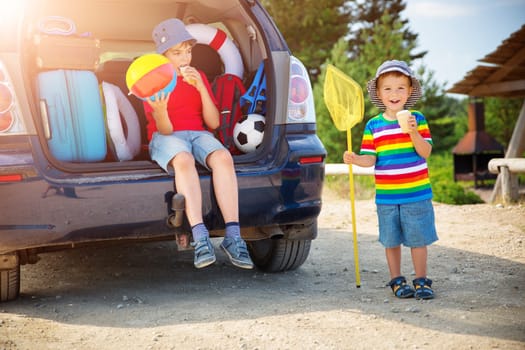 Boy resting in nature in beautiful summer day. child sitting in car filled with traveling accessories and luggage. Travel and vacations concept