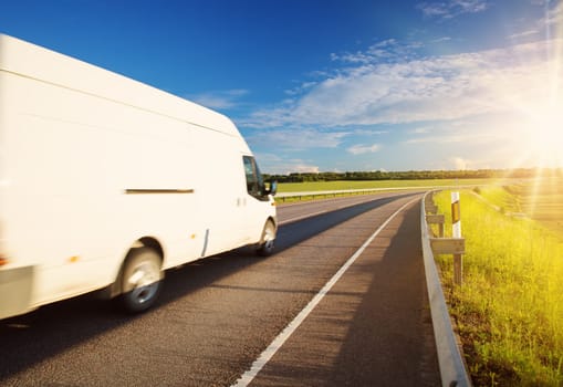 asphalt road on dandelion field with a small truck. white van moving on sunny summer evening on highway. Transportation and delivery concept
