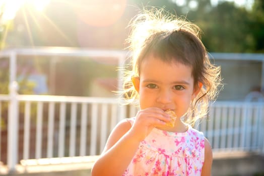 Sweet young girl eating a cookie outdoors at sunset