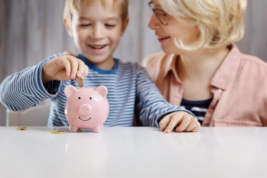 three years old child and young woman sitting at the table with money and piggybank. Happy boy with euro coins. Future childhood and education investment. Finance and savings concept. Son playing with mother