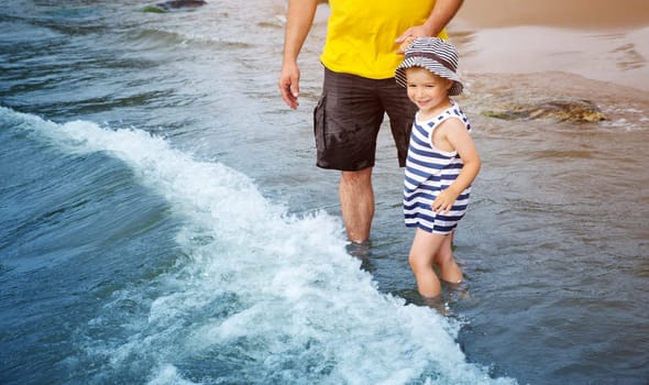 three years old boy with father playing at the beach in the water. Happy child and man on family vacations at sea in summer. Summertime tourism and travel concept