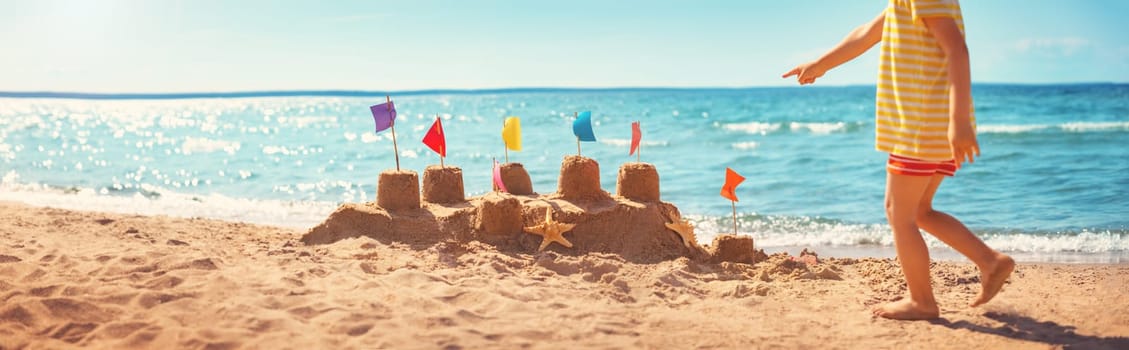 boy building a sandcastle at the beach in summer. Child on vacations at blue sea playing in sand near water and having fun