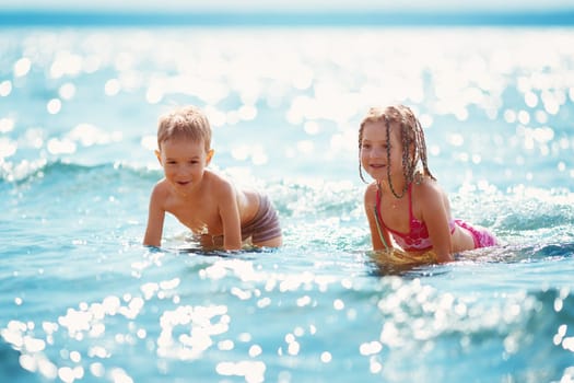 Boy and girl playing on the beach on summer holidays. Children in nature with beautiful sea, and blue sky. Happy kids on vacations at seaside splashing in the water