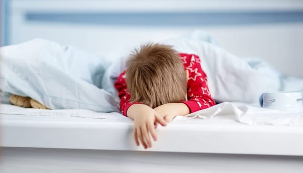 Sleepy boy lying in bed with blue beddings. Tired child in bedroom sleeping. Little kid lying asleep in red pajamas