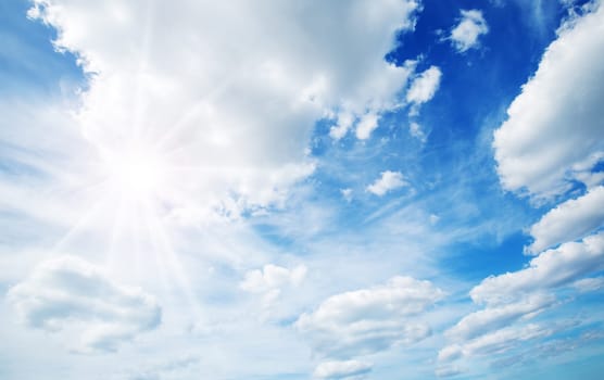 white fluffy clouds on blue sky in summer on sunny day with sunlight. Beautiful cloudscape background with sun