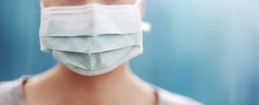 young woman in medical face protection mask indoors on blue background. Sick person
