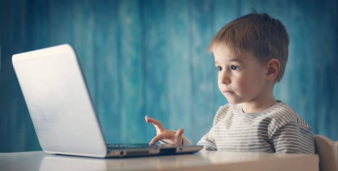 happy five years old child sitting with a laptop at table. Smiling boy working at personal computer