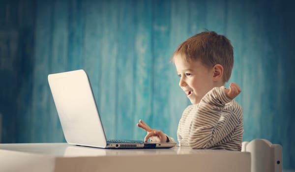 happy five years old child sitting with a laptop at table. Smiling boy working at personal computer