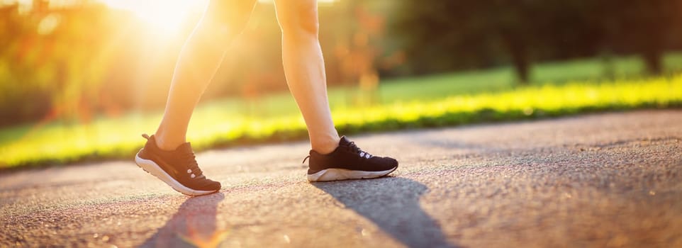 Young woman running in the park. Active person walking outdoors at the dusk in summer on asphalt road