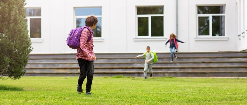 Children with rucksacks standing in the park near school. Pupils with books and backpacks outdoors