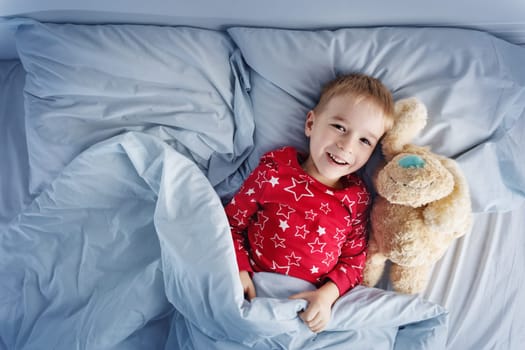 Sleepy boy lying in bed with white beddings. Tired child in bedroom sleeping. Little kid lying asleep with toy