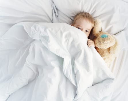 Sleepy boy lying in bed with white beddings. Tired child in bedroom sleeping. Little kid lying asleep with toy