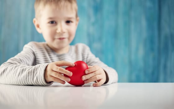 Cute little child holding red heart in hands. Love, care and health concept