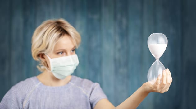 young woman in medical face protection mask indoors on blue background. Sick person