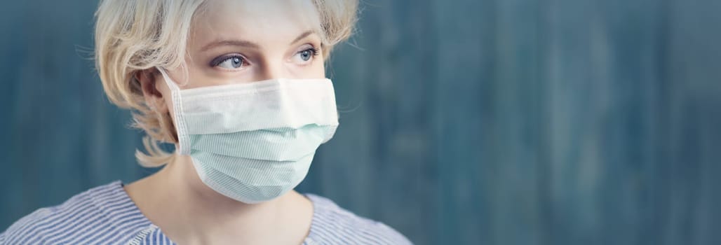 young woman in medical face protection mask indoors on blue background. Sick person
