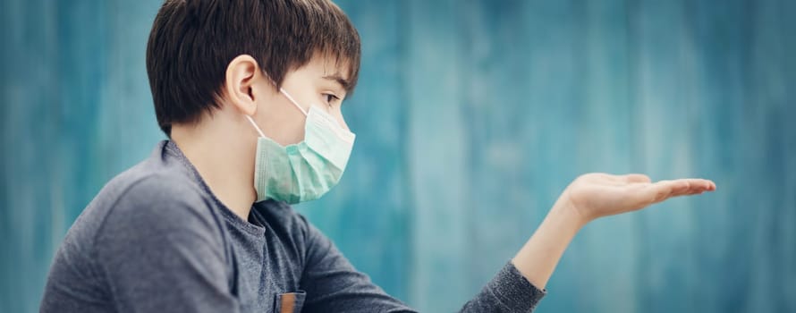 boy in medical face protection mask indoors on blue background. Sick child showing virus