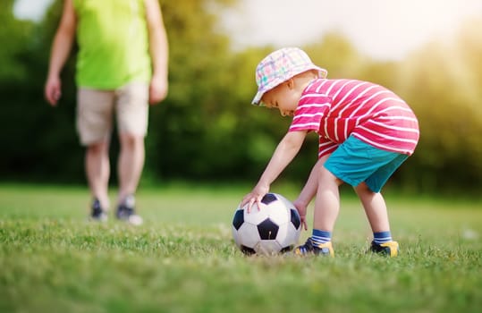 Little boy playting football on the field with gates. Active child in summer with ball