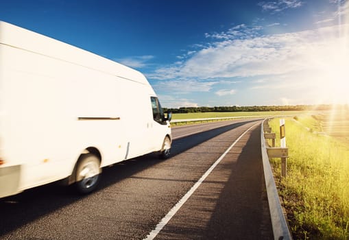 asphalt road on dandelion field with a small truck. white van moving on sunny summer evening on highway. Transportation and delivery concept