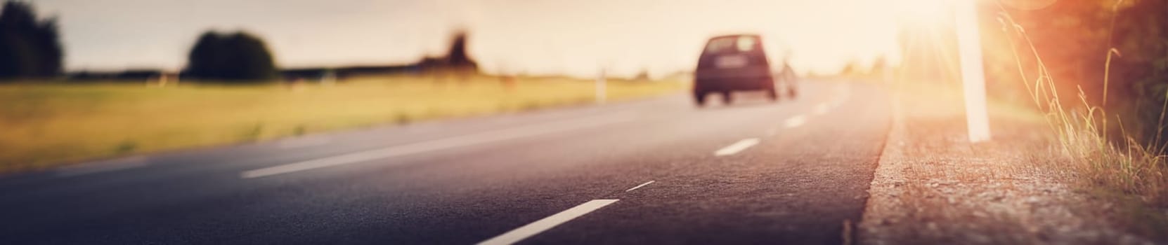 asphalt road view with a blurred car in countryside at beautiful sunset