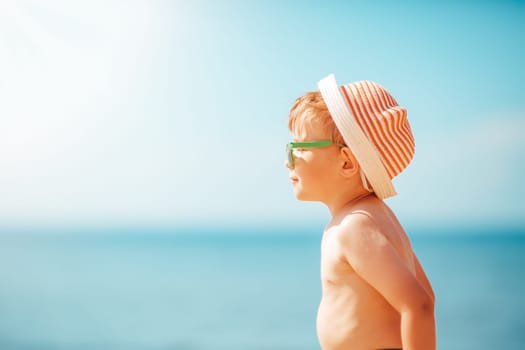 three years old boy smiling at the beach in hat with sunglasses. Relaxed child on vacations at sea getting sunburn