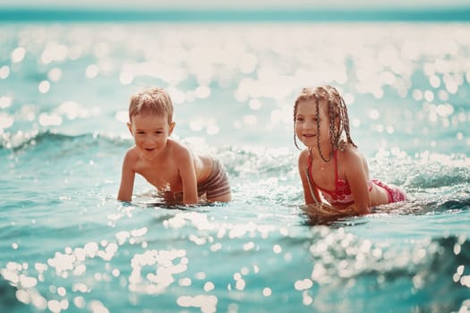 Boy and girl playing on the beach on summer holidays. Children in nature with beautiful sea, and blue sky. Happy kids on vacations at seaside splashing in the water