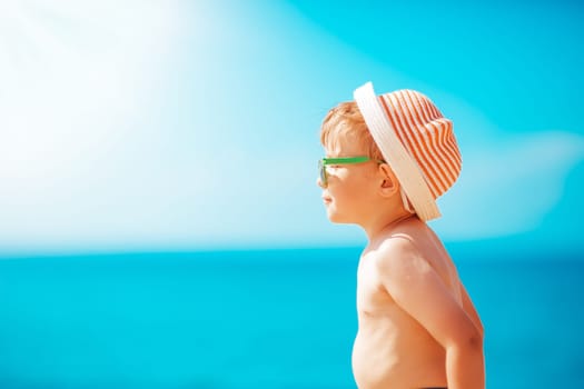 three years old boy smiling at the beach in hat with sunglasses. Relaxed child on vacations at sea getting sunburn