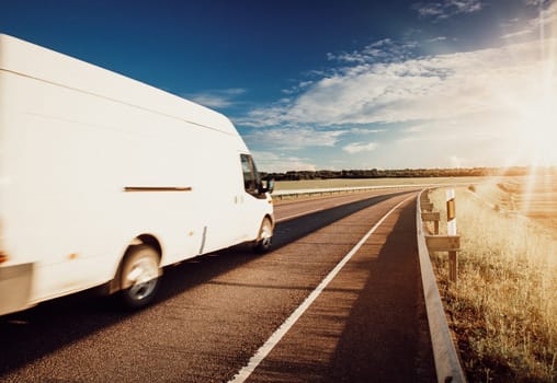 asphalt road on dandelion field with a small truck. white van moving on sunny summer evening on highway. Transportation and delivery concept
