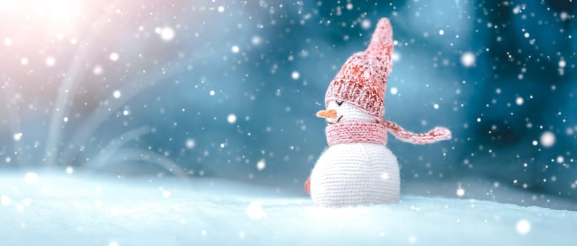 little knitted snowman on soft snow on blue background