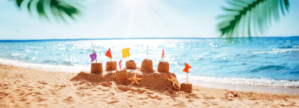 Sandcastle on the blue sea in summertime. Seashore with clean sand on beautiful day in summer. Tropical landscape with palm leaves. Vacations and travel concept