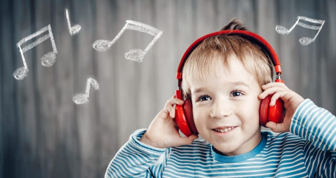 happy little boy on wooden background with red headphones. Child listening music with wireless headset. Musical concept with people