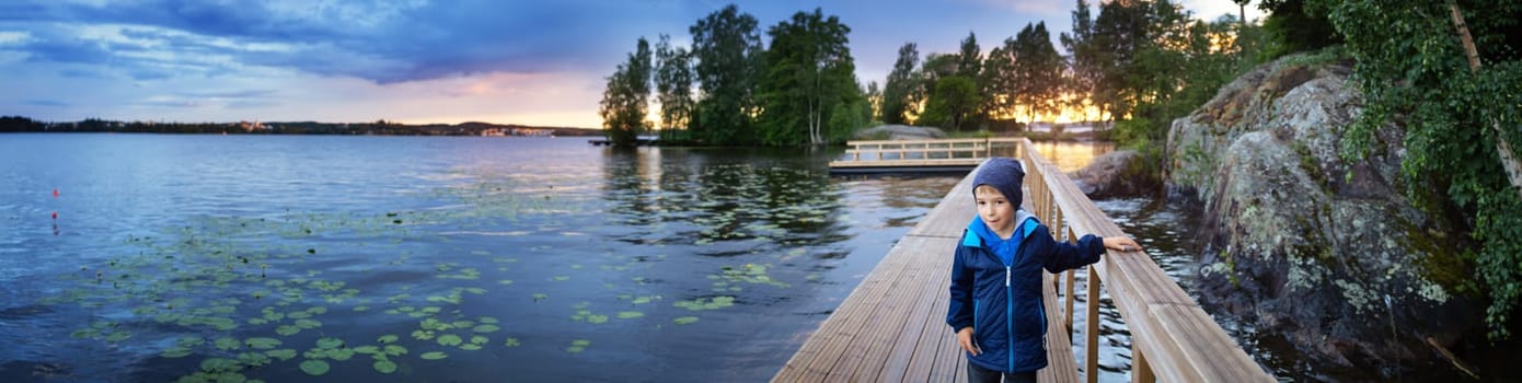 Little boy at the lake in Tampere, Finland. Child stand on the wooden pier near water on the sunset.