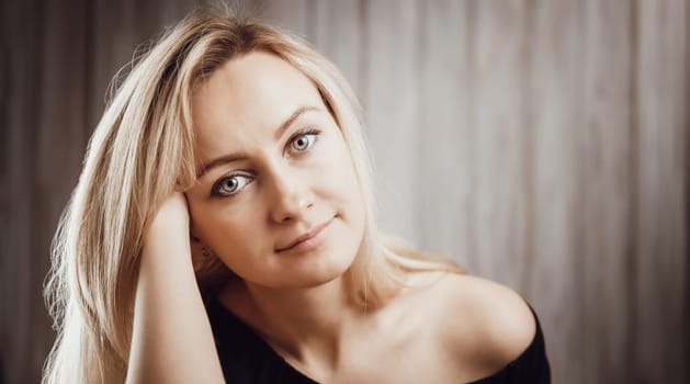 Happy beautiful young blond woman portrait with wooden background. Attractive girl in studio with long hair