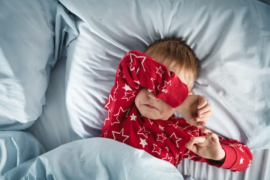 Sleepy boy lying in bed with blue beddings. Tired child in bedroom. Little kid lying awake in red pajamas with toothache