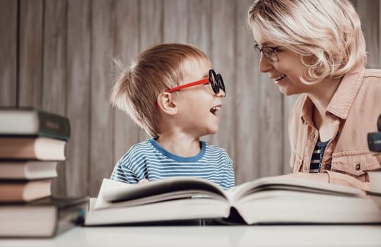 five years old child reading a book at home with mother. Boy in funny glasses studying with mom