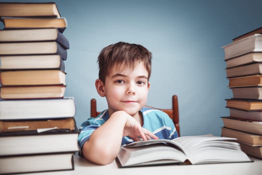 seven years old child reading a book at home. Boy studing at table on blue background
