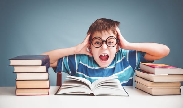 seven years old child reading a book at home. Boy studing at table on blue background