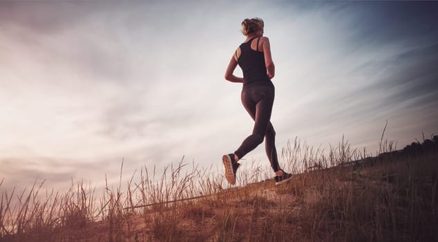 Young woman running on the field near seaside at sunset. Active person outdoors at the dusk in summer