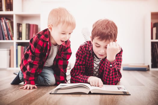 Three years old child and his older brother sitting among books at home. Curious boys reading in white room