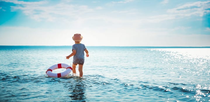 three years old boy playing at the beach in hat. Child with a lifebuoy at sea in summer