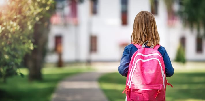 Girl with rucksack infront of a school building. Child with a backpack