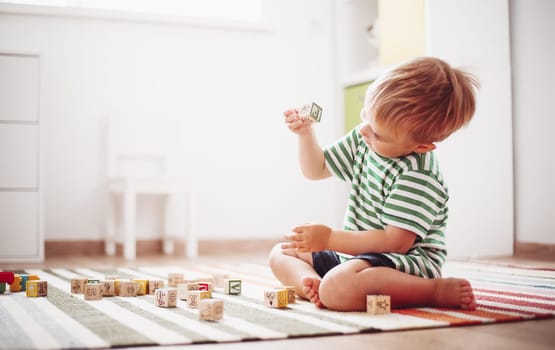 two years old child sitting on the floor. Pretty little boy palying with wooden cubes at home