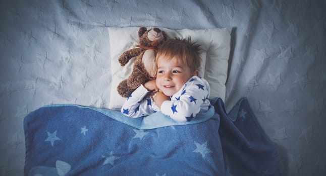 three years old child sleeping in bed on pillow with a teddy bear