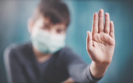 boy in medical face protection mask indoors on blue background. Sick child showing protest