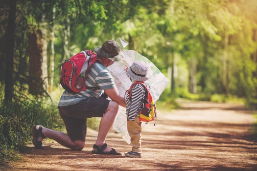 Father and boy going camping with tent in nature. Man with son with backpacks walking in the forest