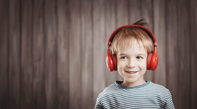 happy little boy on wooden background with red headphones. Child listening music with wireless headset. Musical concept with people