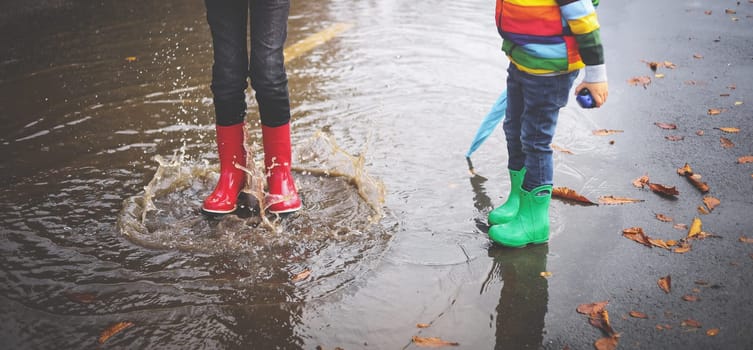 Child walking in wellies and jumping in puddle on rainy weather. Boy under rain in autumn outdoors