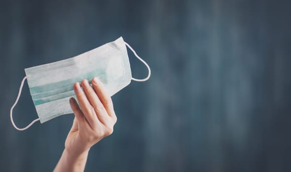 young woman holding face protection mask indoors on blue background. Sick person