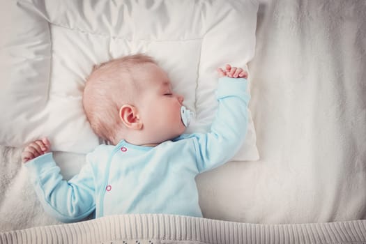 Seven month old baby sleeping on white blanket and pillow. Sleepy child on soft bedding with pacifier